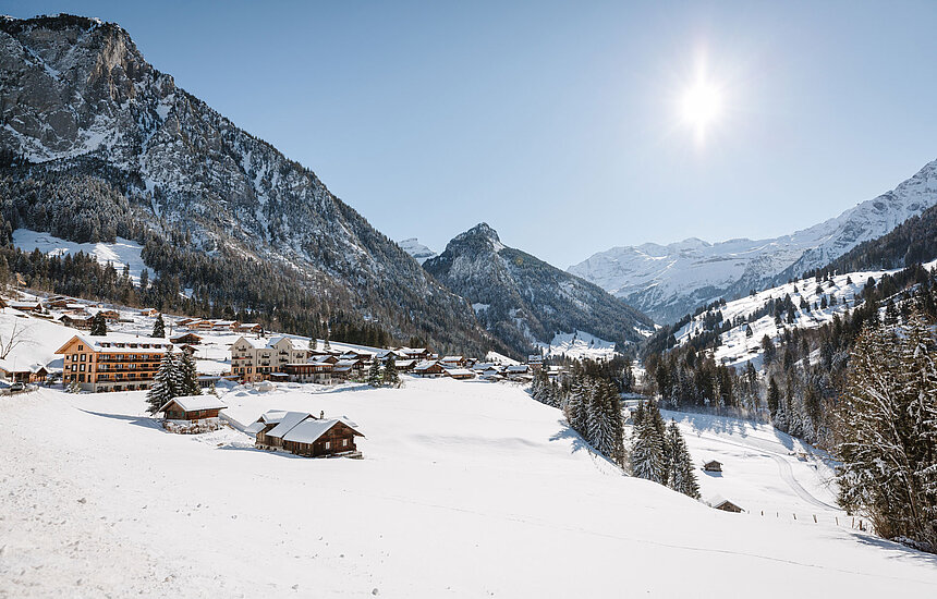 Winterlandschaft mit Chalets im Kientals umgeben von Bergen, stahlblauem Himmel und Sonne.